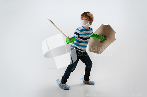 Image of Little caucasian boy as a warrior in fight with coronavirus pandemic, with a shield, a sword and a toilet paper bandoleer, protecting