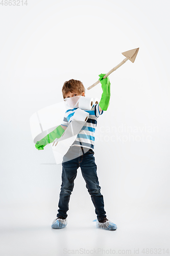 Image of Little caucasian boy as a warrior in fight with coronavirus pandemic, with a face mask, a spear and a toilet paper bandoleer, attacking