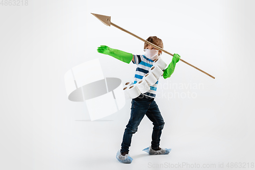 Image of Little caucasian boy as a warrior in fight with coronavirus pandemic, with a face mask, a spear and a toilet paper bandoleer, attacking