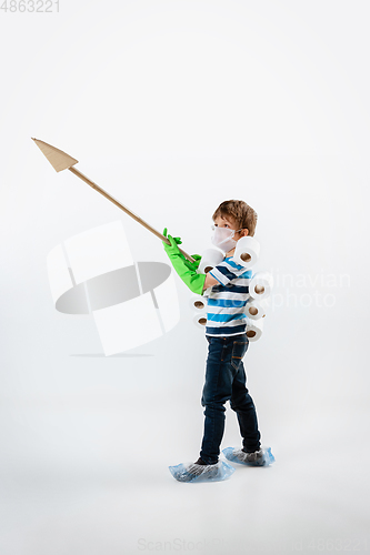 Image of Little caucasian boy as a warrior in fight with coronavirus pandemic, with a face mask, a spear and a toilet paper bandoleer, attacking