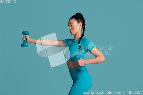 Image of Beautiful young female athlete practicing on blue studio background, monochrome portrait