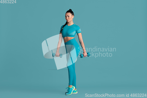 Image of Beautiful young female athlete practicing on blue studio background, monochrome portrait