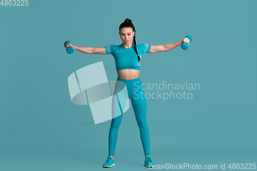 Image of Beautiful young female athlete practicing on blue studio background, monochrome portrait