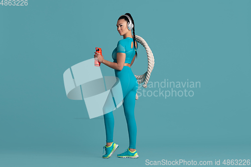 Image of Beautiful young female athlete practicing on blue studio background, monochrome portrait