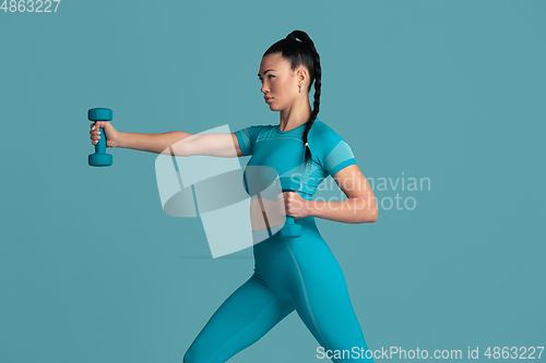 Image of Beautiful young female athlete practicing on blue studio background, monochrome portrait