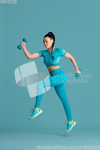 Image of Beautiful young female athlete practicing on blue studio background, monochrome portrait