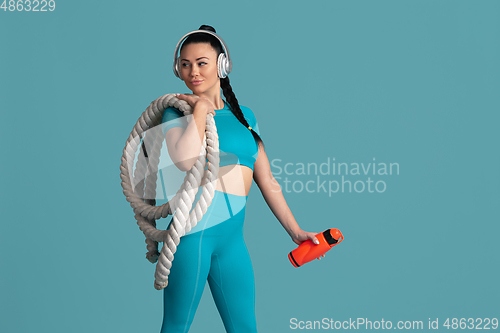 Image of Beautiful young female athlete practicing on blue studio background, monochrome portrait