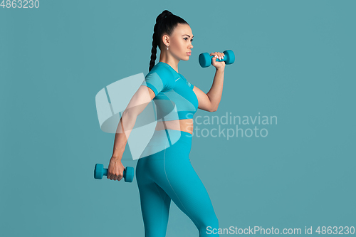 Image of Beautiful young female athlete practicing on blue studio background, monochrome portrait