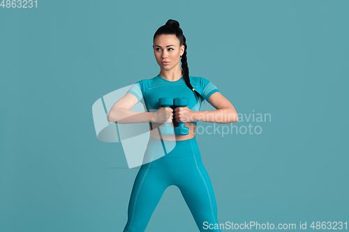 Image of Beautiful young female athlete practicing on blue studio background, monochrome portrait