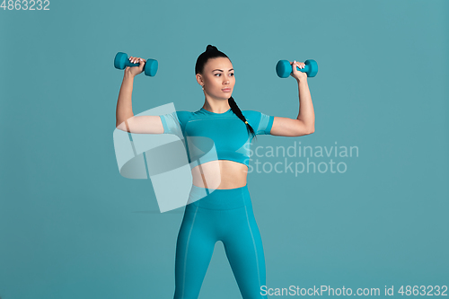 Image of Beautiful young female athlete practicing on blue studio background, monochrome portrait