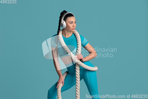 Image of Beautiful young female athlete practicing on blue studio background, monochrome portrait