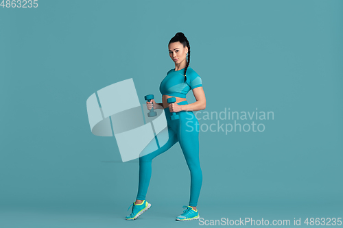 Image of Beautiful young female athlete practicing on blue studio background, monochrome portrait