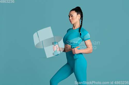 Image of Beautiful young female athlete practicing on blue studio background, monochrome portrait