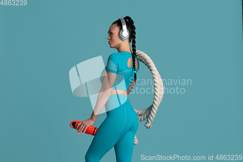 Image of Beautiful young female athlete practicing on blue studio background, monochrome portrait