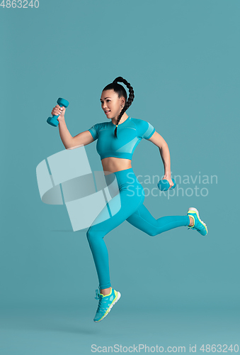 Image of Beautiful young female athlete practicing on blue studio background, monochrome portrait