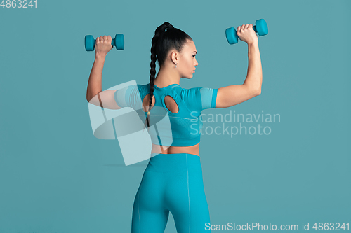 Image of Beautiful young female athlete practicing on blue studio background, monochrome portrait