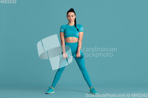 Image of Beautiful young female athlete practicing on blue studio background, monochrome portrait