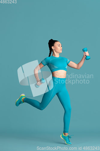 Image of Beautiful young female athlete practicing on blue studio background, monochrome portrait