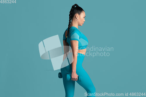 Image of Beautiful young female athlete practicing on blue studio background, monochrome portrait