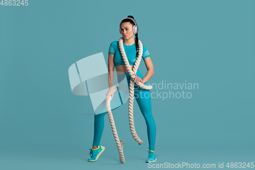 Image of Beautiful young female athlete practicing on blue studio background, monochrome portrait