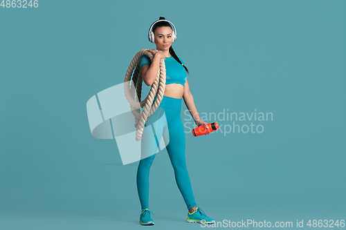 Image of Beautiful young female athlete practicing on blue studio background, monochrome portrait