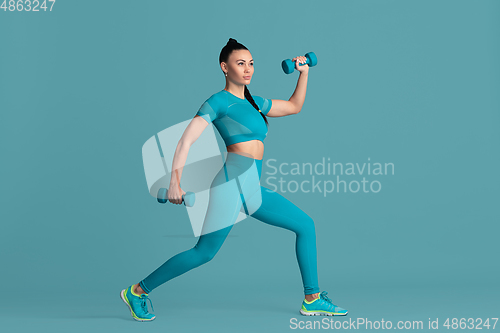 Image of Beautiful young female athlete practicing on blue studio background, monochrome portrait