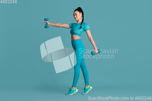 Image of Beautiful young female athlete practicing on blue studio background, monochrome portrait