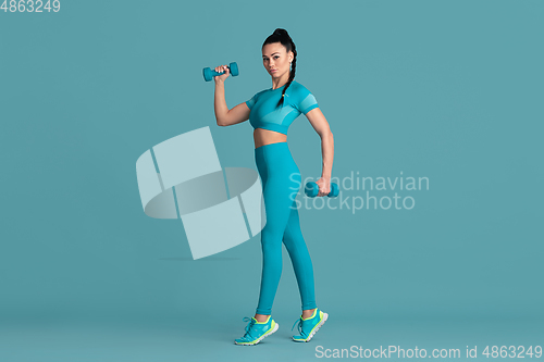 Image of Beautiful young female athlete practicing on blue studio background, monochrome portrait