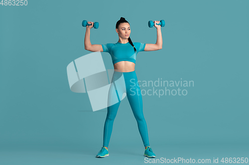 Image of Beautiful young female athlete practicing on blue studio background, monochrome portrait