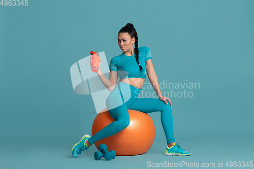 Image of Beautiful young female athlete practicing on blue studio background, monochrome portrait