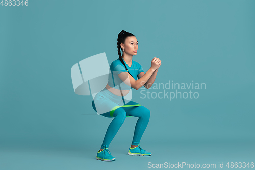 Image of Beautiful young female athlete practicing on blue studio background, monochrome portrait