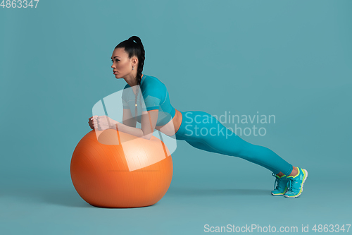 Image of Beautiful young female athlete practicing on blue studio background, monochrome portrait