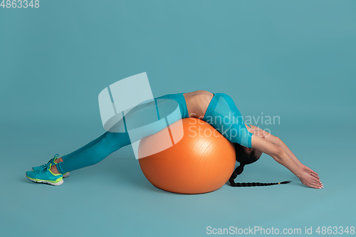 Image of Beautiful young female athlete practicing on blue studio background, monochrome portrait