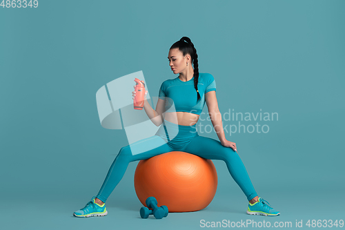 Image of Beautiful young female athlete practicing on blue studio background, monochrome portrait