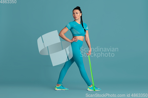 Image of Beautiful young female athlete practicing on blue studio background, monochrome portrait