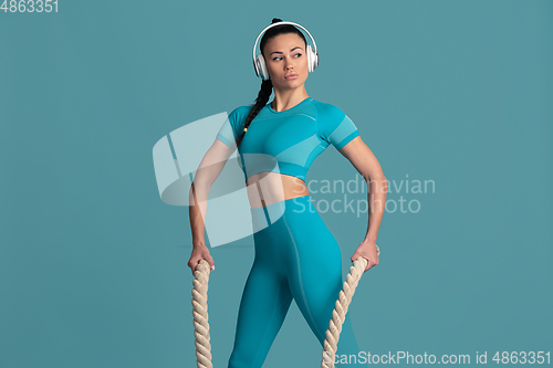 Image of Beautiful young female athlete practicing on blue studio background, monochrome portrait