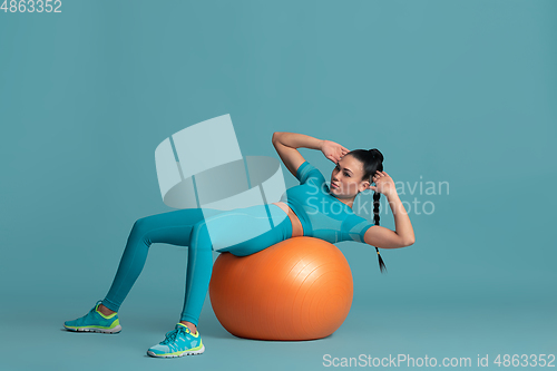 Image of Beautiful young female athlete practicing on blue studio background, monochrome portrait