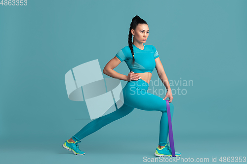 Image of Beautiful young female athlete practicing on blue studio background, monochrome portrait