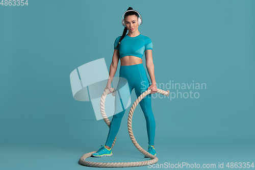 Image of Beautiful young female athlete practicing on blue studio background, monochrome portrait