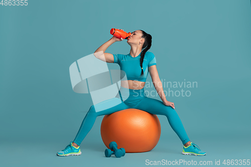 Image of Beautiful young female athlete practicing on blue studio background, monochrome portrait