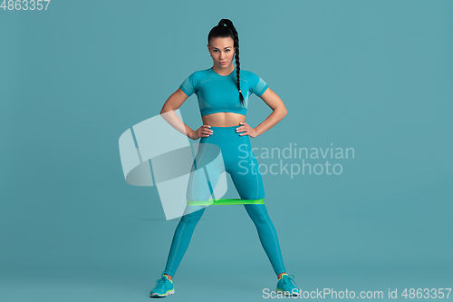 Image of Beautiful young female athlete practicing on blue studio background, monochrome portrait