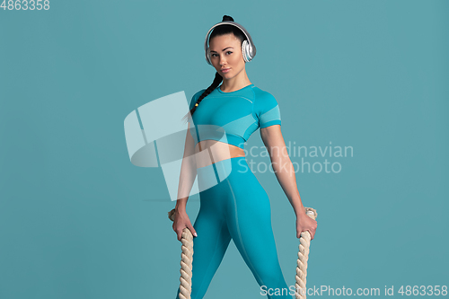 Image of Beautiful young female athlete practicing on blue studio background, monochrome portrait