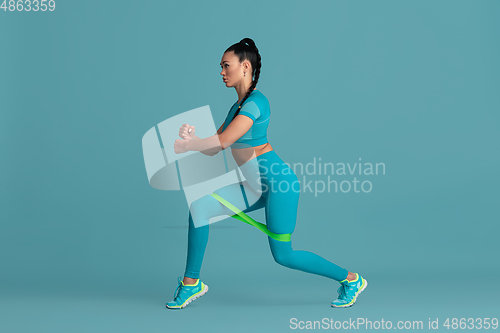 Image of Beautiful young female athlete practicing on blue studio background, monochrome portrait