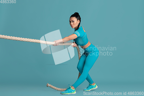 Image of Beautiful young female athlete practicing on blue studio background, monochrome portrait