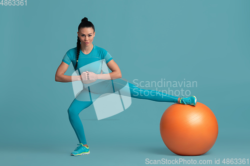 Image of Beautiful young female athlete practicing on blue studio background, monochrome portrait