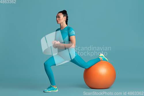 Image of Beautiful young female athlete practicing on blue studio background, monochrome portrait