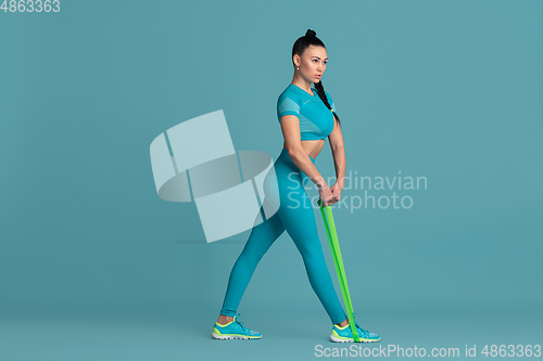 Image of Beautiful young female athlete practicing on blue studio background, monochrome portrait