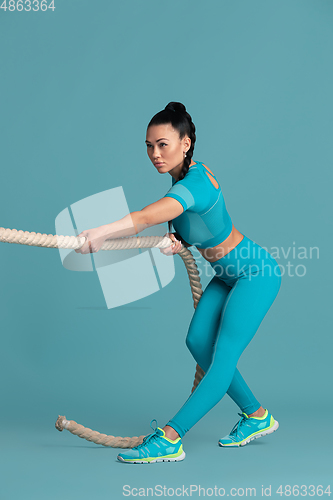 Image of Beautiful young female athlete practicing on blue studio background, monochrome portrait