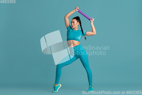 Image of Beautiful young female athlete practicing on blue studio background, monochrome portrait