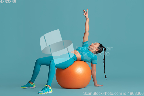 Image of Beautiful young female athlete practicing on blue studio background, monochrome portrait